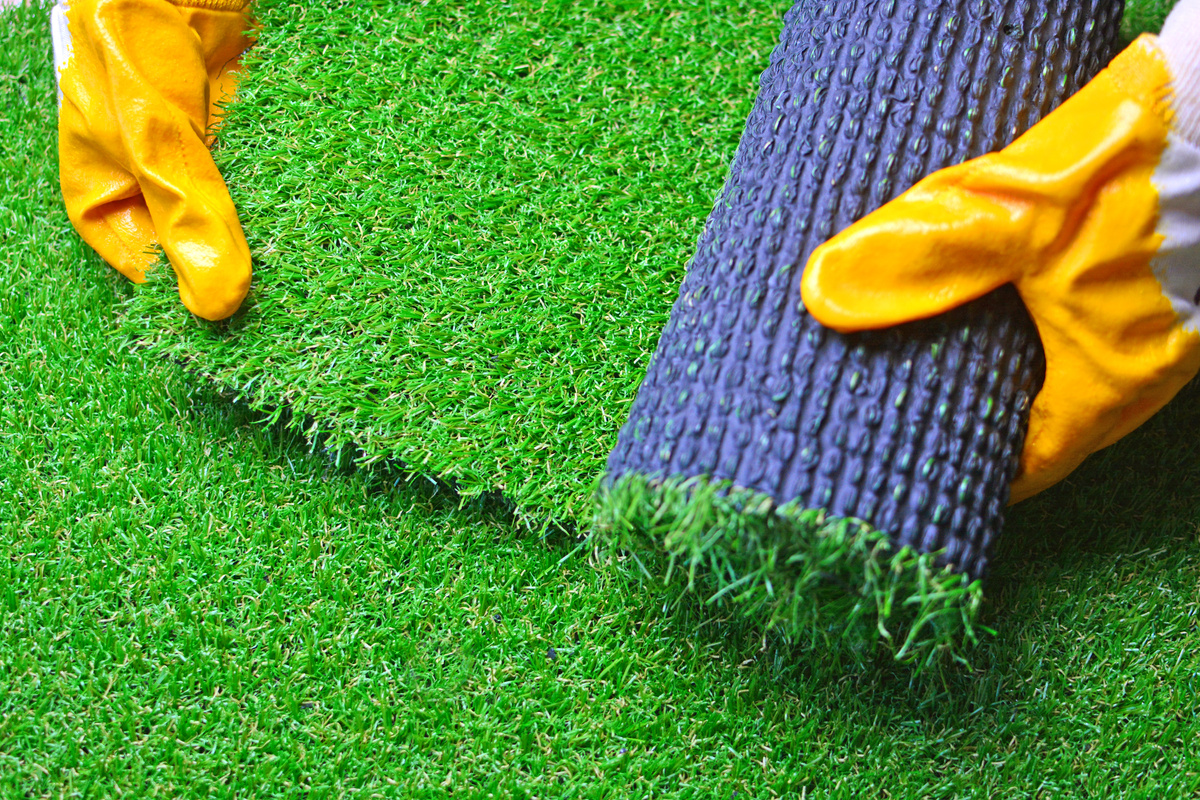 Worker hands with an artificial grass roll. Artificial turf laying.